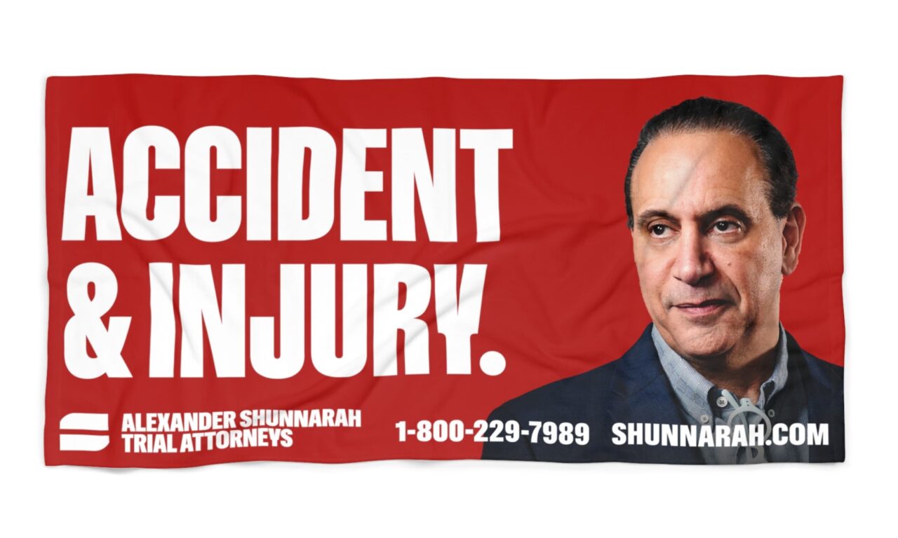 Red Alexander Shunnarah Trial Attorneys Towel reading "Accident & Injury" featuring the face of Alexander Shunnarah, web address shunnarah.com, and phone number: 1-800-229-7989