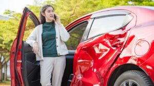A woman leans against her car door and talks on the phone. Her car is dented. This photo portrays a common situation for a diminished value claim in Alabama.