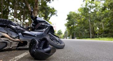 A motorcycle lays on the side of the road with an abandoned helmet.