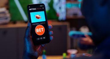 A young man plays with a sports betting app on his phone.