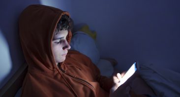 Teenager using a smartphone lying in bed late at night, playing games, watching videos online, and scrolling the screen. Children's screen addiction. Screen Addiction in Youth.