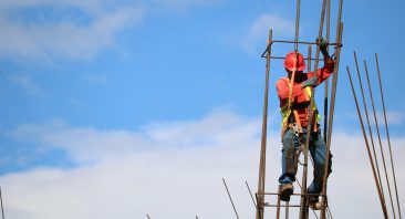 A construction worker climbs a ladder on a job site; if they fall, then they may require an Alabama workers' compensation attorney to recover benefits.