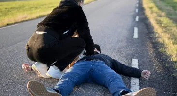 A person lays on a road and receives chest compressions; they may need a Birmingham pedestrian accident attorney if this took place in the city.