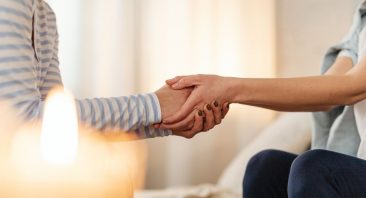 Two anonymous figures hold hands in front of a candle, illustrating the compassion needed for a civil lawsuit after sexual assault.