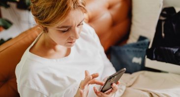 A frustrated woman taps on her phone screen, portraying the common scenario of dealing with insurance dispute tactics.