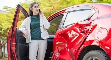 A woman leans against her car door and talks on the phone. Her car is dented. This photo portrays a common situation for a diminished value claim in Alabama.