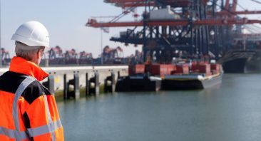A dockworker in safety gear on a shipping pier with cargo containers in the background. Dockworker injury claims fall under the Longshore and Harbor Workers Act.
