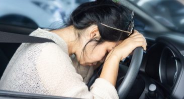 A woman leans her forehead against a steering wheel, implying that she may need to know dram shop law.