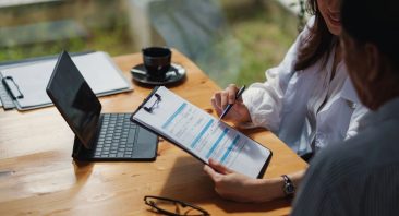 Two people discuss car and insurance documents, illustrating how much insurance goes up after an accident.