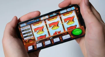 A person holds their phone in front of the camera, showing a gambling app, implying gambling addiction.