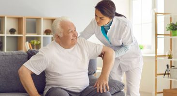 A caregiver gently supports an elderly nursing home resident, illustrating pressure ulcer prevention and care.