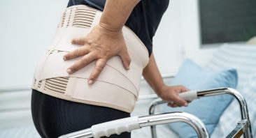 A person wears a back brace and bends over in pain, portraying a type of spinal cord injury.