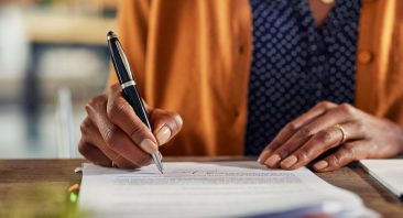 A woman signs a personal injury demand letter on a desk with a pen, illustrating a settlement demand.