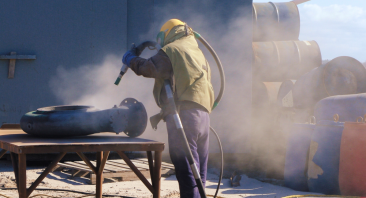 A construction worker operates a sandblaster, portraying the concept of what to do after inhaling dust at a worksite.