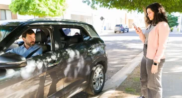 A concerned passenger stands on a shoulder road next to a rideshare vehicle. This is when someone would need a Lyft accident lawyer.